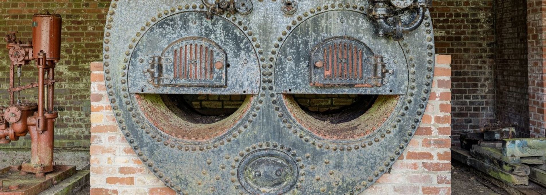A circular, cast iron boiler on brick supports. It has two doors that look like eyes in the front.