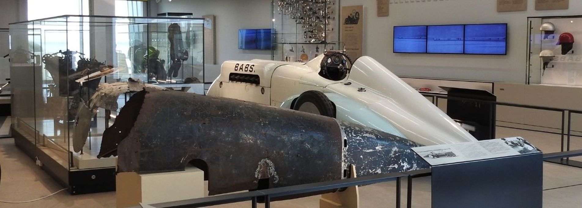 Panoramic photo of a large gallery space with Babs and car parts visible in the centre