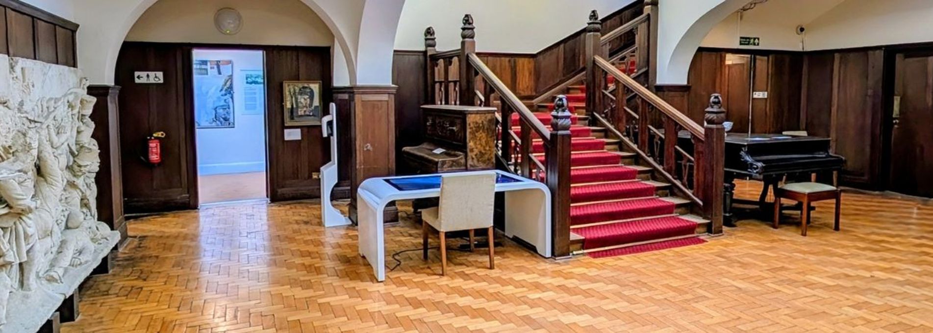 Panoramic photo of a spacious, wood panelled room, with a broad staircase in the centre