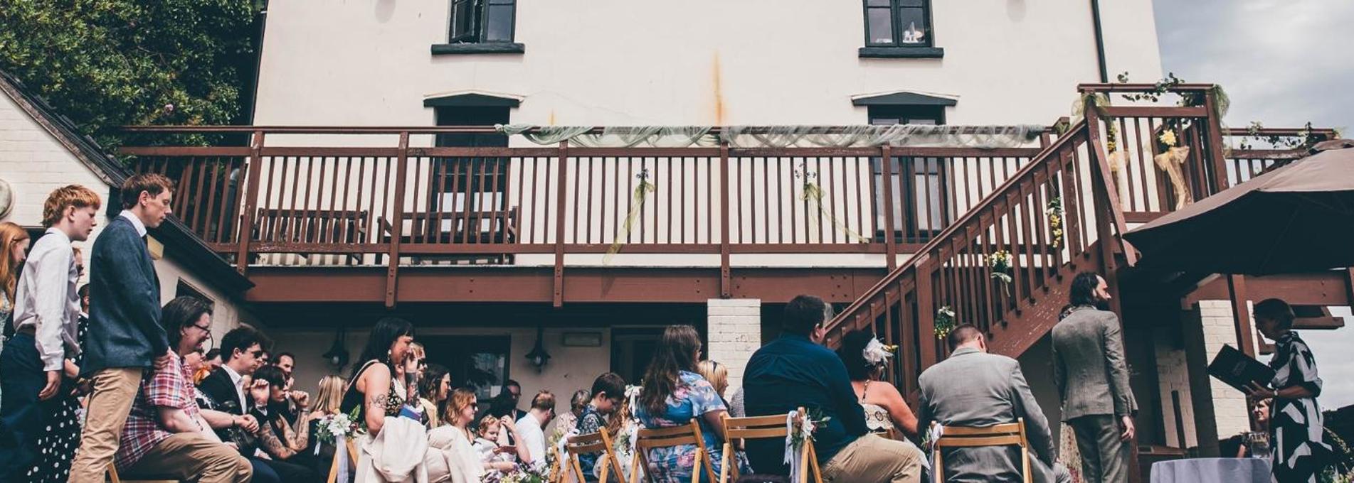 Smartly dressed people stand outside the Dylan Thomas Boathouse witnessing a wedding ceremony