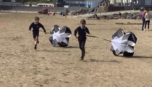 Two children run along Pendine beach with small parachutes trailing behind
