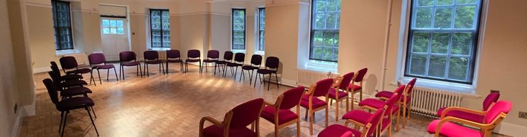 Large room with windows along the right wall and the rear. Empty chairs laid out for a musical performance.