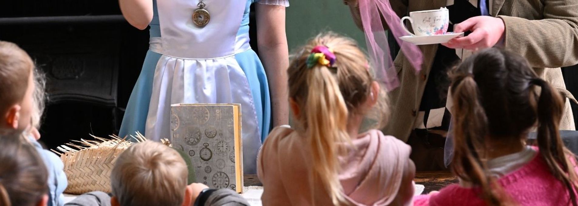 A row of children from behind who are watching a scene with two actors
